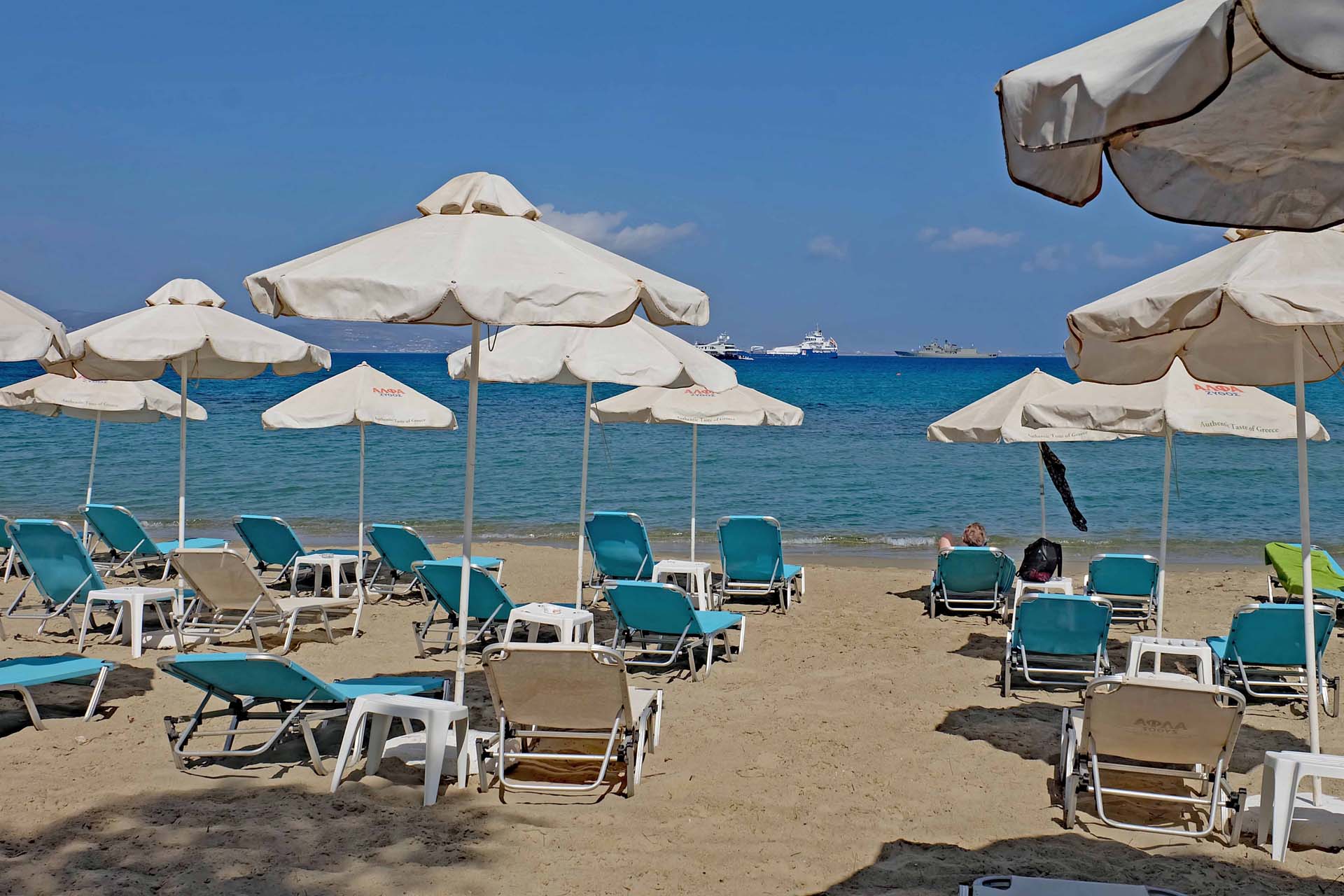 Sonnenliegen und -Schirme am Strand von Agios Georgios. Blick auf das Meer