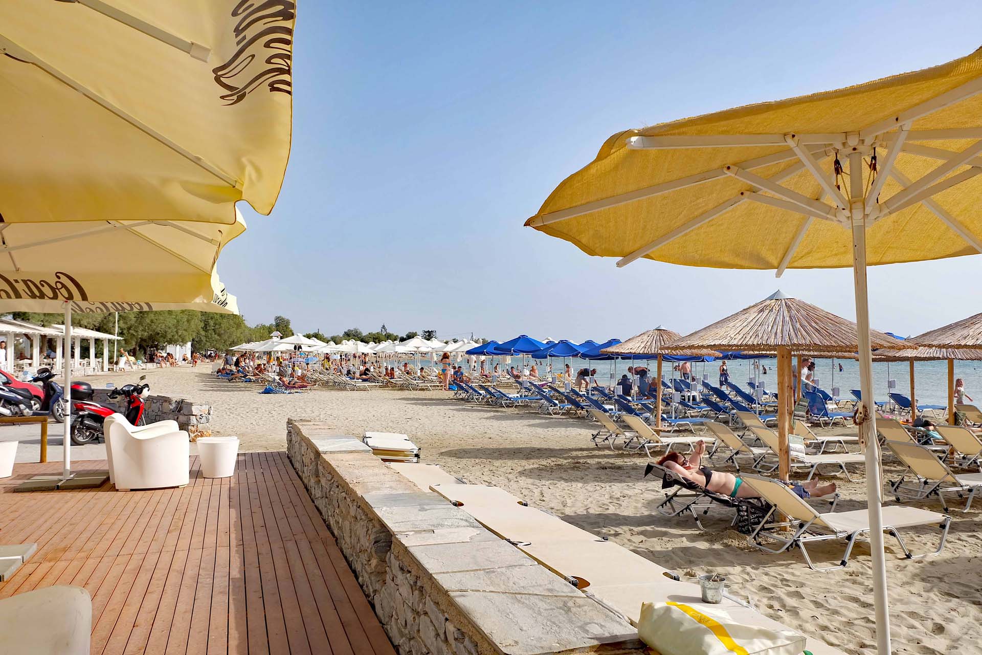 Sonnenliegen und -Schirme am Strand von Agios Georgios. An der Bar